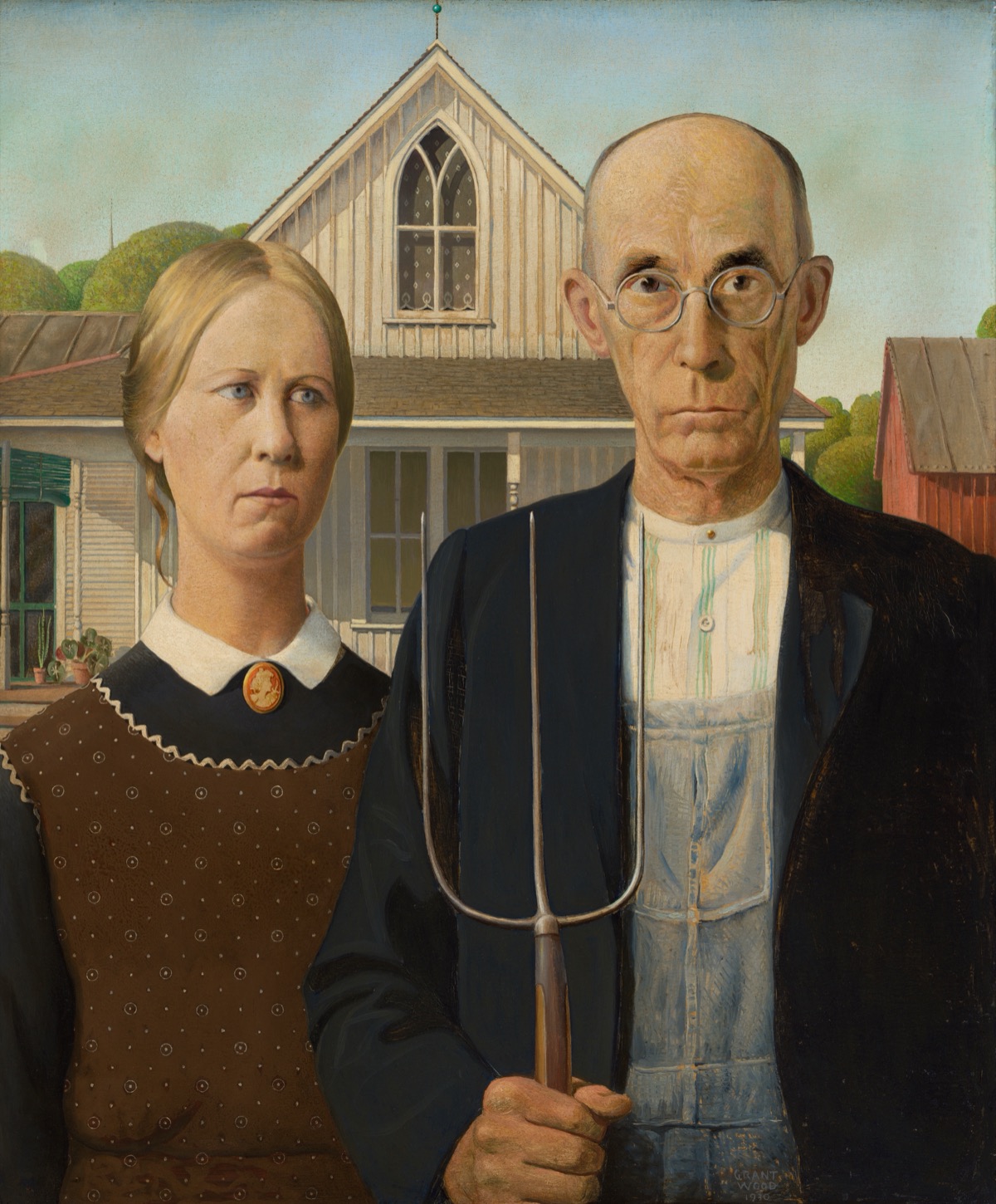 American Gothic by Grant Wood: a bald farmer in round glasses, overalls and a dark jacket holds a pitchfork upright beside a woman with pulled-back hair, a brown patterned apron and a cameo brooch, in front of a white wooden house with a pointed Gothic window and a red barn.