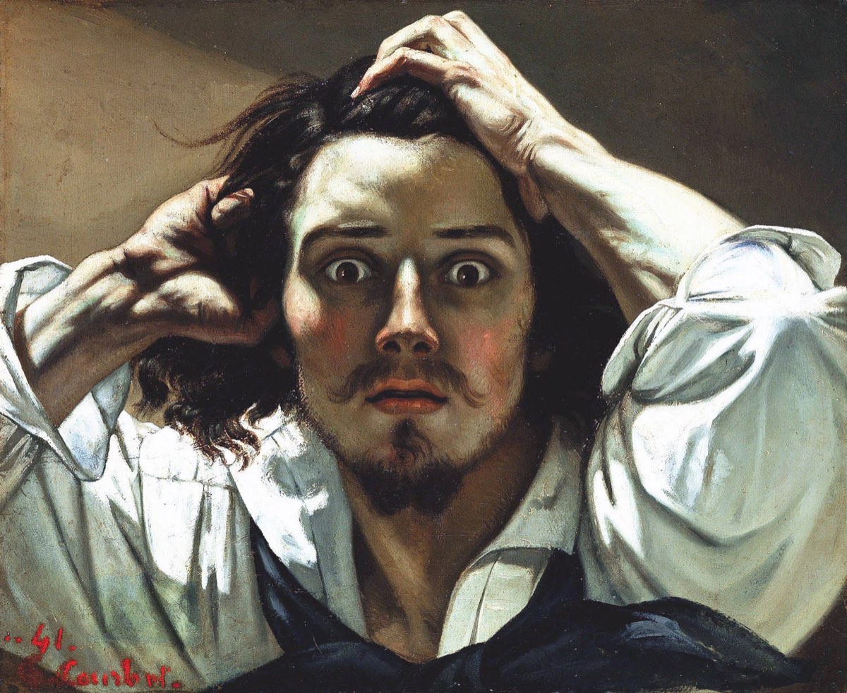 The Desperate Man by Gustave Courbet: a young man with long dark hair and a moustache stares wide-eyed out of the frame, both hands pulling at his hair, in a loose white shirt against a dark background.